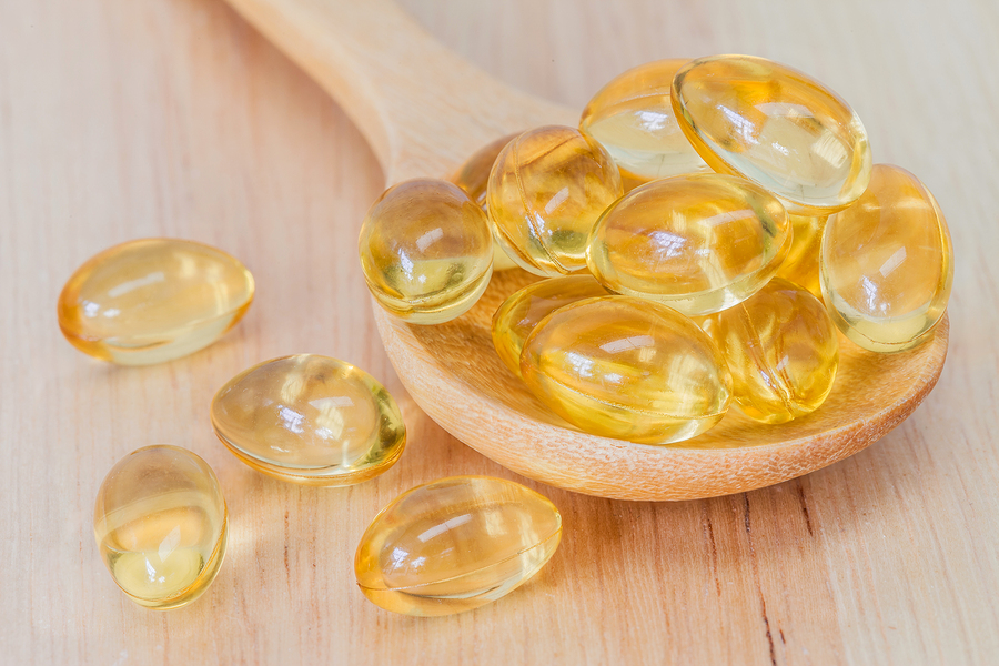 Fish oil supplement capsule on wooden spoon and wooden backgroun